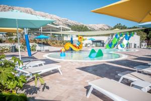 a pool with a water park with tables and umbrellas at Valamar Camping Baška in Baška