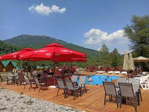 a pool with chairs and red umbrellas and people swimming at Camp Sutjeska in Tjentište
