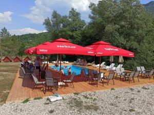 a pool with red umbrellas and chairs and people sitting around it at Camp Sutjeska in Tjentište