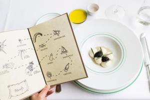 a person holding a book next to a plate of food at La Foresteria Planeta Wine Resort & Beach Club in Menfi