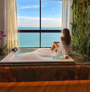 Hotel Espadarte في إيريري: امرأة جالسة في حوض الاستحمام تنظر من النافذة
