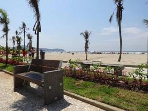 um banco de parque junto a uma praia com palmeiras em Apartamento Primeira Quadra Da Praia na Praia Grande