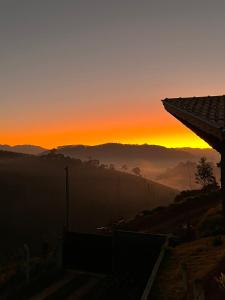 a sunset in the mountains with the sun setting in the background at Chalés Água azul in Santo Antônio do Pinhal
