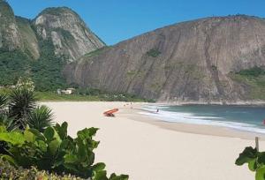 a beach with people on the sand and a mountain at Apto novo em Icarai in Niterói