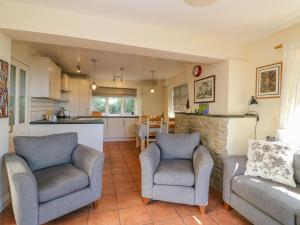 a living room with two chairs and a kitchen at Mimosa Cottage in Swyre