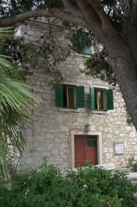 ein Steingebäude mit grünen Fenstern und einer roten Tür in der Unterkunft Apartments by the sea Sepurine, Prvic - 4237 in Prvić Šepurine