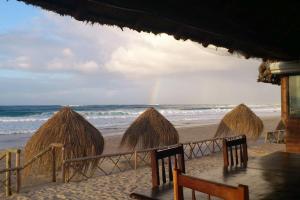 a group of straw huts on a beach with a rainbow at Casa Coco Palmeira in Inhambane