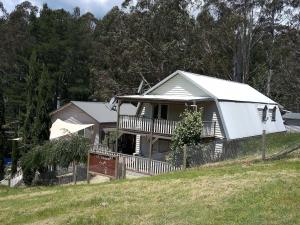 a white house with a porch on a hill at Beautiful Dutch Barn style country house in Merrijig (base of Mt Buller). in Merrijig