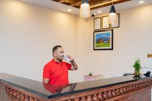 Ein Mann, der hinter einer Theke steht und am Telefon redet. in der Unterkunft Madhuban Hotel in Kathmandu