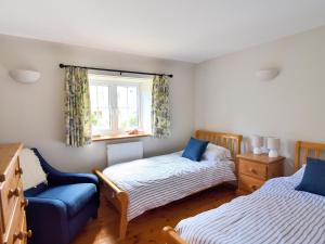 a bedroom with two beds and a chair and a window at Damson Tree Cottage in Bridport