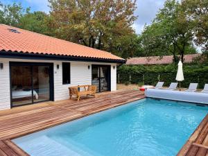 a swimming pool with a wooden deck and a house at Cap Ferret - Villa Sérénité - piscine, proche Océan et Bassin, classée 4 étoiles Meublé de tourisme in Lège-Cap-Ferret