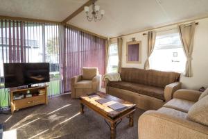 a living room with a couch and a tv and a table at Great 6 Berth Caravan By The Beach At California Cliffs In Scratby Ref 50010l in Great Yarmouth