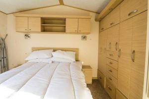 1 dormitorio con 1 cama blanca grande y armarios de madera en Great 6 Berth Caravan By The Beach At California Cliffs In Scratby Ref 50010l en Great Yarmouth