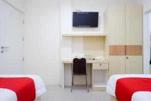 a bedroom with two beds and a desk with a television at RedDoorz Plus near Pasar Gede Solo in Solo