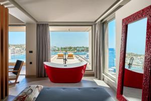 Castello Infinity Suites - Adults Only في أغيا بيلاغيا: حوض استحمام أحمر كبير في غرفة مع نافذة كبيرة