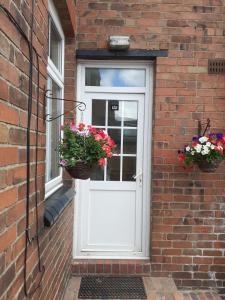 białe drzwi z kwiatami na ceglanym budynku w obiekcie Rose Cottage w mieście Telford