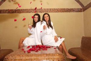 two women in white robes sitting on a bed with roses at Incanto Family Hotel in Sevlievo