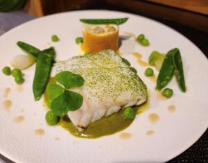 a white plate with a piece of fish and green peas at Auberge La Meuniere in Thannenkirch