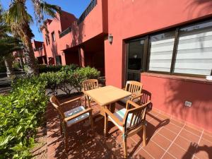 a wooden table and chairs in front of a red building at Corralejo Happy Place, precioso apartamento con piscina in Corralejo