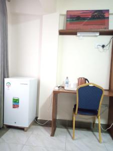 Zimmer mit einem Schreibtisch, einem Stuhl und einem kleinen Kühlschrank. in der Unterkunft Logmma Regency Hotel in Kakamega