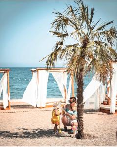 a woman and a child sitting under a palm tree on the beach at premium park apart otel in Kemer