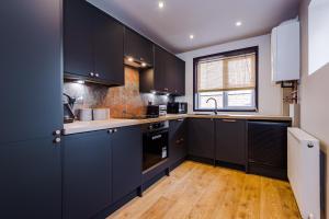 een keuken met zwarte kasten en een houten vloer bij Four Bedroom Urban Home hosted by MCR Dens in Manchester