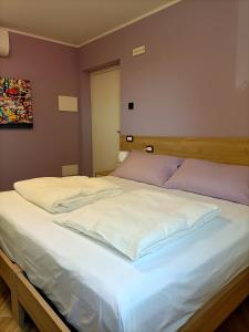 a large bed with white sheets and purple pillows at B&B Rio Rai in Gemona del Friuli