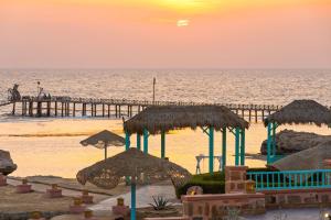a beach with umbrellas and a pier at sunset at Radisson Blu Resort El Quseir in Quseir