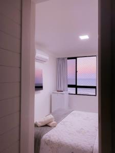 a white bedroom with a bed and a window at Acomodação aconchegante à beira- mar in Natal