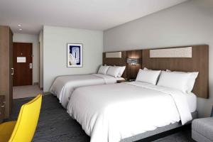 two beds in a hotel room with a yellow chair at Holiday Inn Express & Suites - Hollister by IHG in Hollister