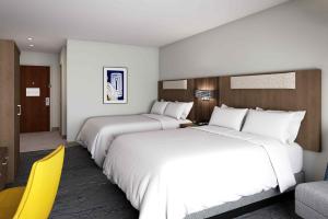 two beds in a hotel room with a yellow chair at Holiday Inn Express & Suites - Hollister, an IHG Hotel in Hollister