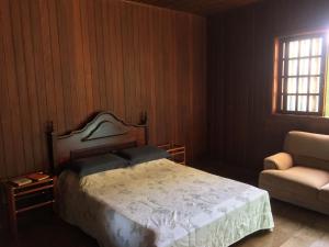 a bedroom with a bed and a chair and a window at Chalé Aconchegante in Maria da Fé