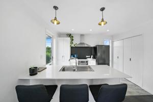 a white kitchen with a sink and some chairs at Treasure on Tuscan - Martinborough Holiday Home in Martinborough