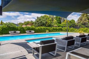 einen Pool mit Stühlen, einem Tisch und einem Sonnenschirm in der Unterkunft Treasure on Tuscan - Martinborough Holiday Home in Martinborough 