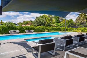 a swimming pool with chairs and a table and an umbrella at Treasure on Tuscan - Martinborough Holiday Home in Martinborough 