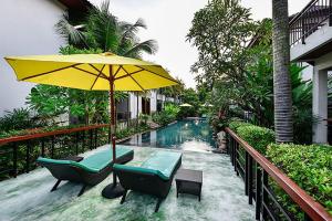 a patio with a yellow umbrella and chairs and a pool at Coco Retreat Phuket Resort and Spa - SHA Plus in Chalong 