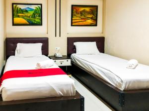 two beds in a room with paintings on the wall at RedDoorz At Hotel Gajah Mada Palu in Palu