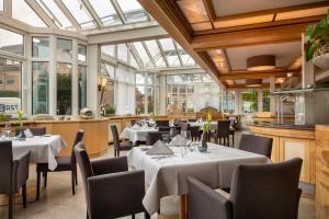 un restaurante con mesas y sillas blancas y ventanas en Hotel Elisenhof Mönchengladbach, en Mönchengladbach