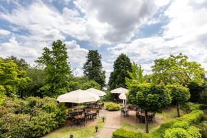 un patio con tavoli e ombrelloni in un parco di Hotel Elisenhof Mönchengladbach a Mönchengladbach