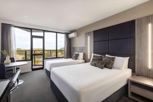 a hotel room with two beds and a desk and a window at Rydges South Park Adelaide in Adelaide