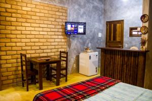 a room with a bed and a table and a refrigerator at Chalé 03 Itaipu Vale da Colina Niterói in Niterói