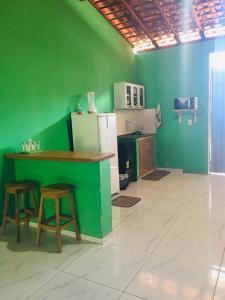 a kitchen with a green wall with a counter and stools at Rosana House Bem estar em Barreirinhas Ideal para 5 pessoas in Barreirinhas