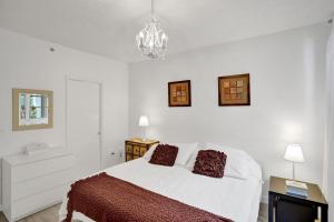 Habitación blanca con cama y lámpara de araña. en Yacht Club Newly renovated parking included en Aventura