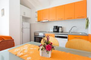 eine Küche mit orangefarbenen Schränken und einem Tisch mit Blumen darauf in der Unterkunft Valentina Apartment and Studio in Vantačići
