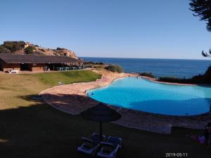 a swimming pool with two chairs next to the ocean at Cozy summer house in Alvor