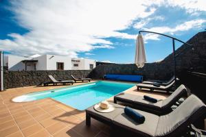 a swimming pool with chaise lounge chairs and an umbrella at Villa Vista Reina - Luxury 6 Bedroom - Heated Pool- Views - Pool Table - Vista Lobos - Playa Blanca in Playa Blanca