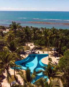 a resort swimming pool with palm trees and the ocean at Pousada Vila do Beco in Arraial d'Ajuda