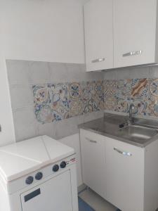 uma cozinha com armários brancos e um lavatório e azulejos em Casa Vittoria em Roccella Ionica