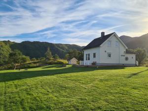a white house on a lawn with mountains in the background at Lauvåsstua-Charming house by the sea in Bøstad