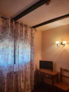 Habitación con cortina, TV y mesa. en Hotel rural la casona de Tamaya en Tamajón